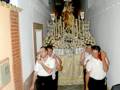 Una imagen de una procesión religiosa con una estatua de la Virgen en el centro, rodeada por personas que parecen estar participando en un acto religioso. La decoración y la vestimenta sugieren una celebración o fiesta patronal.