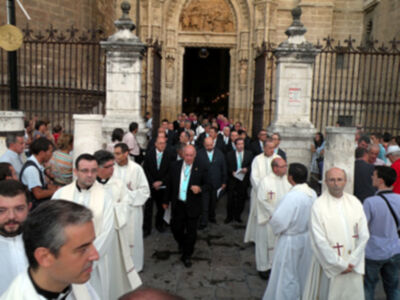 Procesión religiosa con sacerdotes y fieles en una plaza histórica.