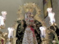 Virgen María en una iglesia, vestida con un manto blanco y rodeada de luces.