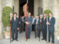 Hombres en trajes formales con palos de procesión, posando en un patio de edificio histórico.