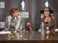 Entrevista en el Teatro Quintero, con dos personas sentadas frente a micrófonos y copas de vino, con un fondo que incluye el nombre del teatro y una ilustración de un hombre con sombrero.