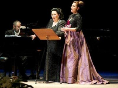 Concierto de ópera con dos cantantes en escena y pianista en el fondo.