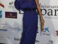 A una mujer con un vestido largo azul marino y una máscara de carnaval en la cara, posando frente a un fondo con logos y logotipos de diferentes empresas.