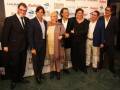 Grupo de personas posando en un evento, con una pancarta de fondo que menciona "Los Alpes".