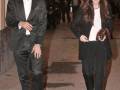 Elegante pareja caminando por la calle, ambos vestidos con trajes negros.