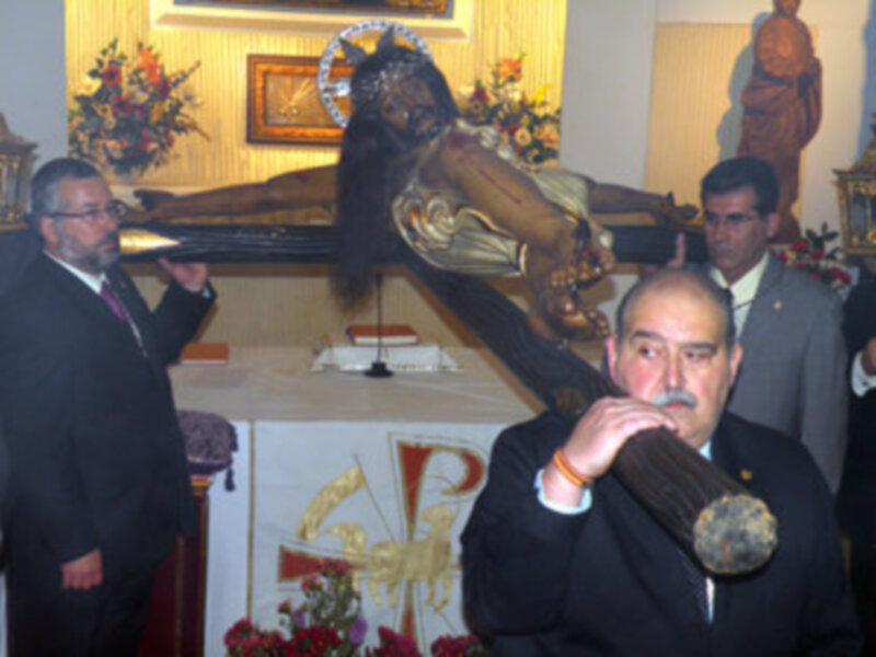 Un hombre sostiene un instrumento musical antiguo en una iglesia, rodeado por flores y decoraciones.