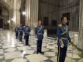 Guardias en uniforme azul y dorado, con escudos de armas, en una sala con suelo de mármol y columnas.