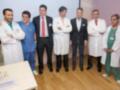 Grupo de médicos y profesionales de salud en un entorno médico, posando para una foto de grupo. El fondo muestra una sala de espera con muebles y una pared con un cartel informativo.