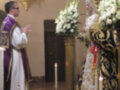 Imagen de una ceremonia religiosa en un templo, con un sacerdote y una persona vestida de blanco en el altar. La imagen muestra detalles como velas, flores y vestimenta tradicional.