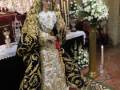 Procesión de la Virgen con vestimentas ornamentales y flores blancas en un entorno religioso.