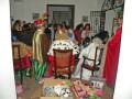 Una escena festiva con personajes disfrazados de Reyes Magos, sosteniendo regalos y juguetes en una habitación decorada con adornos navideños.