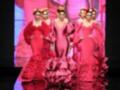 Desfile de moda flamenca con modelos en vestidos de color rosa y detalles de volantes, en un escenario con iluminación dramática.