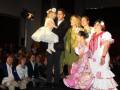 Una familia feliz en un desfile de moda, con una niña pequeña vestida con un traje blanco y otro niño con un traje rosa y blanco.