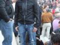 Un hombre con una chaqueta negra y jeans rotos se encuentra en el centro de la imagen, rodeado por una multitud. La escena parece ser al aire libre en un lugar con muchos espectadores, posiblemente durante una actividad pública o deportiva.