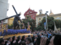 Procesión religiosa en una ciudad, con una imagen de Cristo en la cruz y una multitud de personas observando.