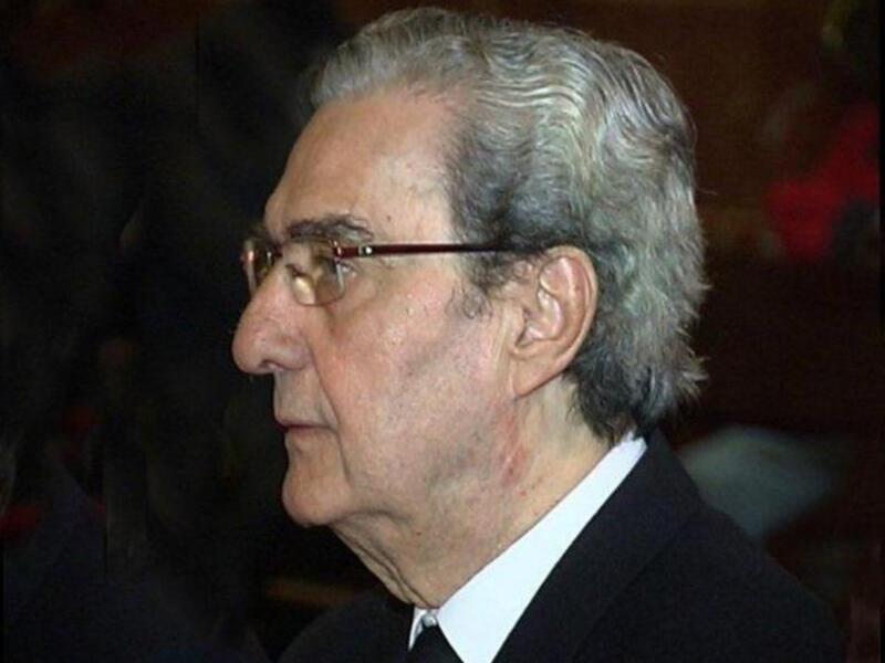 Retrato de perfil de un hombre maduro con cabello gris y gafas, vistiendo traje y corbata.