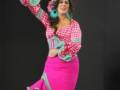 Una mujer vestida con un traje de flamenca rosa y verde, realizando una danza tradicional española.
