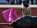 Un torero con capa y espada lucha contra un toro negro en una plaza de toros. La gente observa desde el lado.