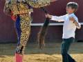 Un torero en traje tradicional se prepara para el toreo, mientras un niño se acerca con curiosidad y respeto.