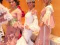 Tres mujeres vestidas con trajes de flamenca posan juntas en un evento formal. La imagen muestra detalles de sus vestidos y accesorios, como flores en la cabeza y joyas.
