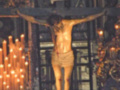 Imagen de Jesús crucificado en una iglesia, rodeado por velas encendidas y decoraciones navideñas.