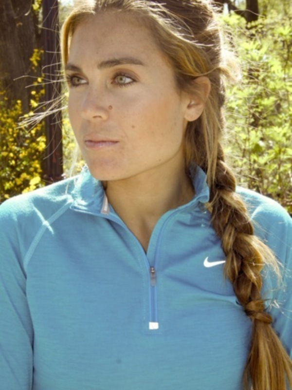 Retrato de mujer con trenza y camiseta deportiva azul en un entorno natural.