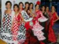 Una fila de mujeres vestidas con trajes tradicionales flamencos, incluyendo vestidos rojos y negros con volantes blancos y negros.