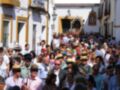 Festividad en la calle, con una procesión y personas con sombreros típicos de la región. La imagen muestra una celebración festiva en un pueblo andaluz, con una procesión religiosa y una multitud de personas participando en la celebración.