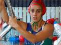 Una jugadora de waterpolo en acción, con un casco rojo y verde, en una piscina.