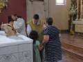 Una imagen de una iglesia donde se puede ver a una persona vestida de blanco, posiblemente un sacerdote, bendiciendo a una niña en el altar. La iglesia tiene vitrales y una silla de madera en el fondo.