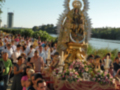 Fotografía de una procesión religiosa con una imagen de la Virgen María en el centro, rodeada de flores y acompañada por una multitud de personas en un ambientesoleado.