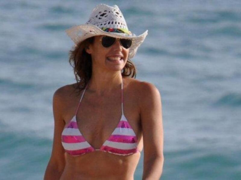 Una mujer con bikini rosa y blanco, sombrero de paja y gafas de sol, disfrutando del mar.