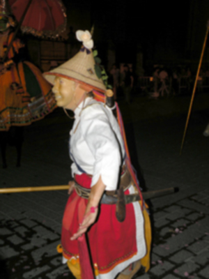 Personaje en traje tradicional con sombrero y escudo, participando en una procesión nocturna.
