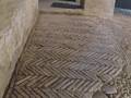 Restos arqueológicos de un suelo de mosaicos romanos en zigzag, con piedras y restos de estructuras antiguas.