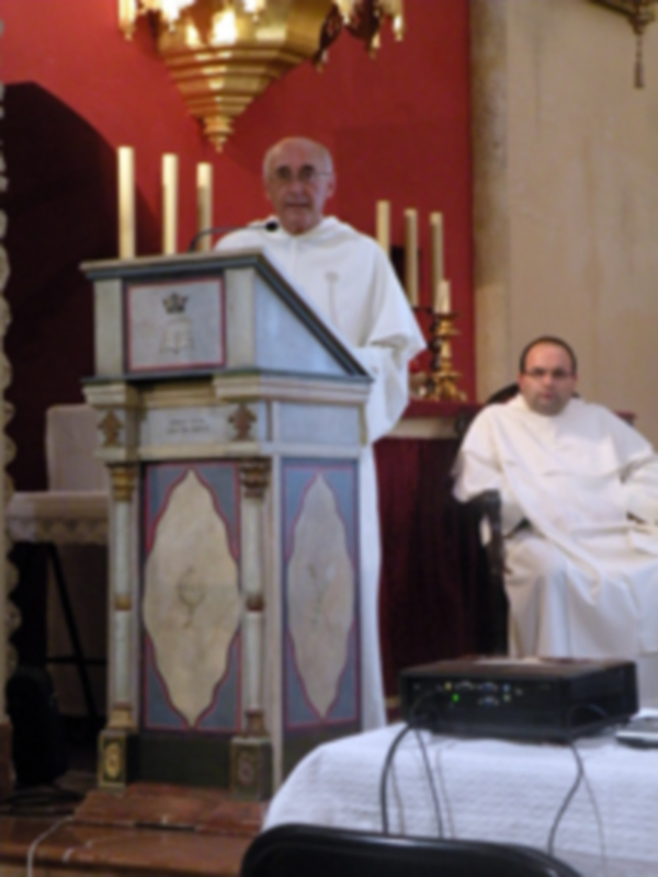 Dos sacerdotes en una iglesia, uno frente a un púlpito con decoración y otro sentado. La imagen muestra una escena religiosa o de oración, con un fondo rojo y detalles dorados.
