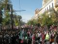 Una multitud en una protesta, con banderas y pancartas, frente a edificios históricos.