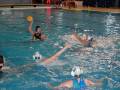 Jugadores de waterpolo en acción, con un jugador lanzando la pelota hacia el arco contrario.