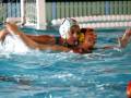 Dos nadadoras en acción durante un partido de waterpolo, con una jugadora intentando atrapar la pelota mientras otra se prepara para defender.
