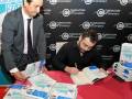 Dos hombres en una firma de libros, uno con corbata y otro firmando un libro. Fondo con logotipo de la Fundación Cofares.