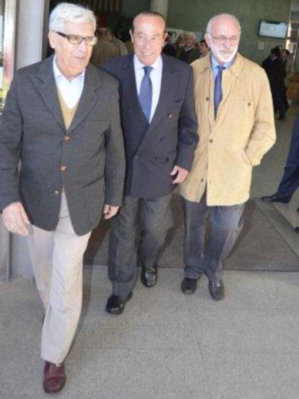Tres hombres caminando juntos, vestidos con trajes y chaquetas, en un entorno urbano.