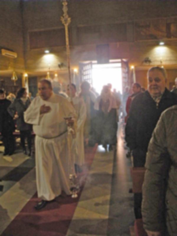 Una iglesia con un hombre en blanco rezando, otros fieles observan. La atmósfera es serena y reverente.