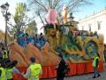Desfile de carnaval con una carroza temática de animales marinos, incluyendo una ballena, un delfín y un pez, con personas vestidas de azul y amarillo en el fondo.