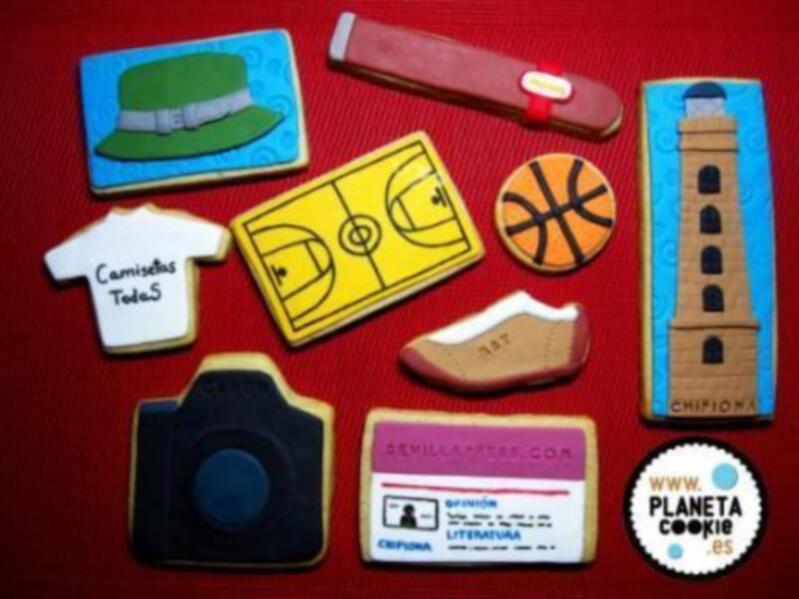 Galletas decoradas con formas y colores que representan diferentes objetos: gorra, baloncesto, camiseta, cámara de fotos, zapato y torre.