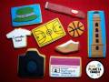 Galletas decoradas con formas y colores que representan diferentes objetos: gorra, baloncesto, camiseta, cámara de fotos, zapato y torre.
