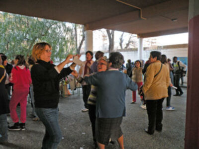 Una imagen de una mujer en el centro, con un grupo de personas a su alrededor. La escena parece ser una reunión o evento público, posiblemente en un parque o plaza. La mujer central parece estar presentando algo a las personas alrededor, posiblemente un informe o una explicación. La gente está atenta y interesada, lo que sugiere un ambiente de aprendizaje o discusión.