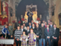 Una imagen de una iglesia con un grupo de personas, algunos vestidos formalmente y otros en trajes más informales. La decoración interior incluye elementos religiosos y una gran arquitectura en el fondo. La imagen parece ser de un evento religioso o ceremonial.