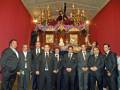 Grupo de hombres en trajes posando frente a una estatua religiosa en un altar.