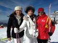 Tres personas en trajes de esquí, dos mujeres y un hombre, posan sonrientes con sus equipamientos. La imagen muestra una estación de esquí en un día soleado, con nieve y montañas al fondo.