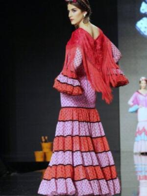 Elegante vestido de flamenca con volantes en tonos rojos y púrpura. La modelo lleva un tocado floral y pendientes largos.