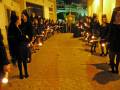 Procesión nocturna con velas en una calle adoquinada, con participantes en trajes negros.